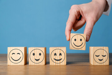 Woman arranging cubes with different emoticons in row on wooden table against light blue background, closeup