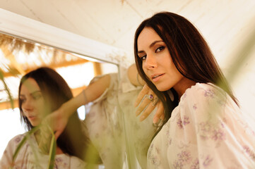 Stylish brunette woman looking at camera near blurred mirror in bungalow 