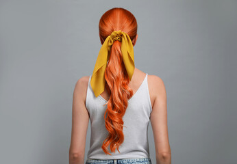 Beautiful woman with long orange hair on light grey background, back view