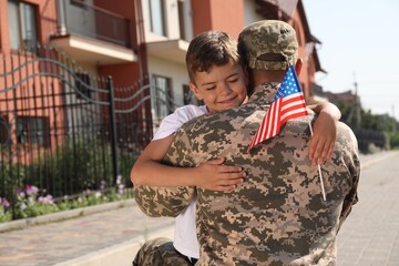 Soldier and his little son with flag of USA hugging outdoors