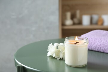 Scented candle, flowers and towel on green table indoors, space for text