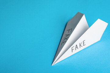 Paper plane with words FAKE on light blue background, top view. Space for text
