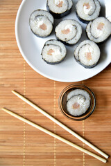 Rice rolls with salmon and cheese with sauce on a plate. Fish sushi sticks. Japanese delicious sushi on a mat.