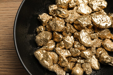 Bowl of gold nuggets on wooden table, top view