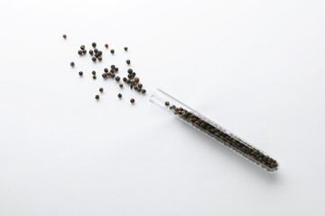 Glass tube with peppercorns on white background, top view