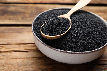 Bowl and spoon with black sesame on wooden table, closeup. Space for text