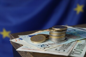Coins and banknotes on wooden table against European Union flag, closeup. Space for text