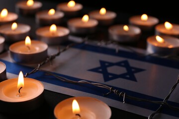 Flag of Israel, barbed wire and burning candles on black background. Holocaust memory day