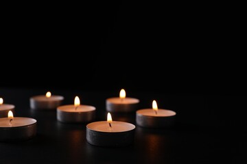 Fototapeta na wymiar Burning candles on black background, space for text. Holocaust memory day