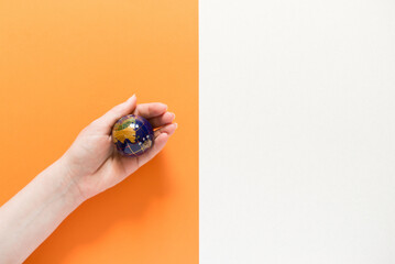 human hand holds a globe on an orange background, space for text.