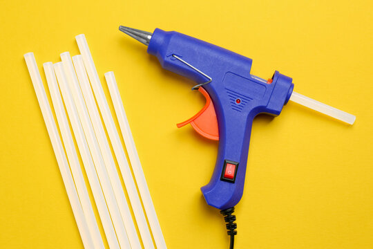 Blue Glue Gun And Sticks On Yellow Background, Flat Lay