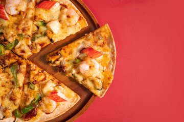 Close up slice of tasty hot baked seafood crispy pizza - mussels, shrimps and kani with chili pepper and melted mozzarella cheese on round pizza dough, on a wooden pizza pan over the red background.