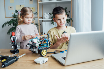 Sister and brother working in pair and looking at the laptop screen while assembling robotics car together. Simple project for engineering class concept