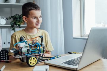 Little attentive boy looking at the laptop screen while assembling robotic car at the table. Kid studying with smart toys and laptop