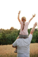 a girl on her father's back, against the background of a yellow field and green trees