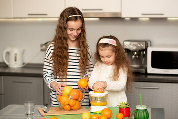Two cute sister girls are making orange fresh juice. They are in the kitchen at home. Family. Fresh fruit. Healthy eating.