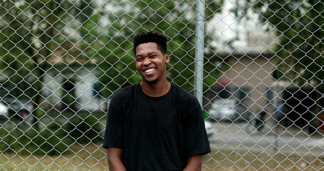 Smiling black guy leaning on metal fence standing casually outside