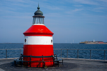 A small red-white-striped lighthouse on the shore. A small island in the background.
