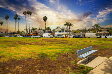 a gorgeous summer landscape in the park with lush green and brown grass and palm trees with a woman sitting on the grass with a baby and parked cars along the street at Shoreline Park in Santa Barbara