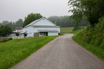 Fototapeta premium Winding country road beside a white barn in the Ohio Amish countryside | Holmes County, Ohio
