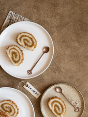 Pieces of biscuit roll with apple jam on a plates next to copper color teaspoons. Brown background, retro paper, flat lay