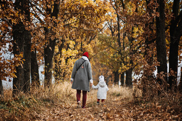 Fototapeta premium Mother and little baby daughter walking together in autumn park, forest. Mother with toddler daughter
