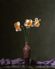 Bouquet of white daffodils in a green glass vase with a cape on a marble table. Spring freshness and aroma. Dark background. Calm still life. Decoration. Four flowers. Comfort, enjoyment at home.