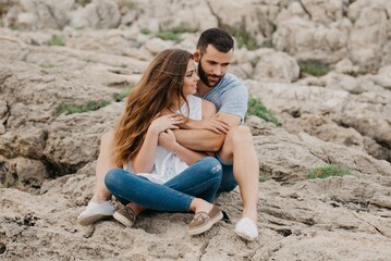 A man is holding his girlfriend while both are sitting on the rocks in Spain