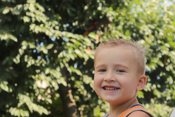 portrait of a cute boy of blonde European appearance close-up against the background of a green garden on a summer day selective focus