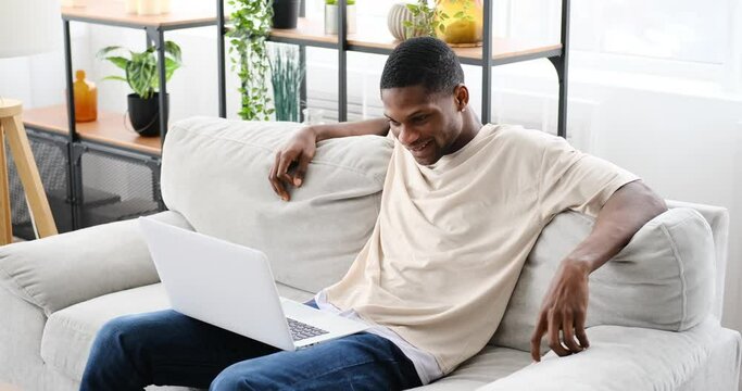 African american man laughing while watching funny movie on laptop at home
