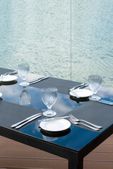 Crystal empty glasses, white plates and cutlery on a table in a beach restaurant. Table setting for a festive dinner.
