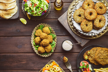 Arabic cuisine; Middle Eastern traditional Falafel dish. Varieties of fresh vegetarian Falafel patties served with green salad, pickles, pita bread, tahini sauce and lemon. Top view with copy space.