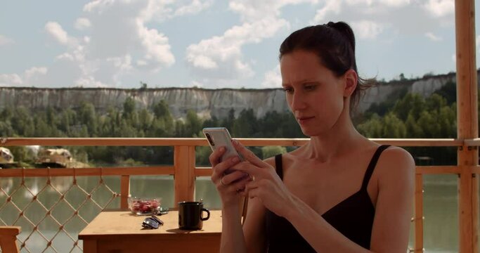 Female comunicate by smartphone with friends while resting on lake on weekend