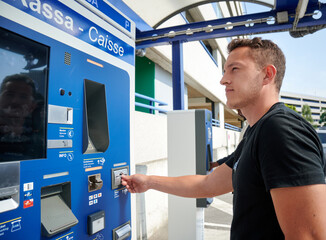 A young male using a ticket vending machine - obrazy, fototapety, plakaty
