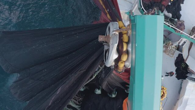 A fishing boat and crew in birds eye while pulling back giant net via a vinch mecanism.