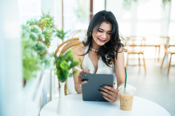 beautiful asian freelance Success people business woman fashion model in summer white sleeveless dress using casual working with tablet for browsing internet, chatting and blogging in coffee shop.