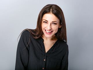 Obraz premium Beautiful young business toothy laughing woman in black shirt looking happy on blue grey background with empty copy space. Portrait