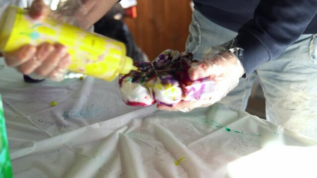Painting of a white T -shirt with yellow paint. Staining T -shirts with your own hands Tie Dye video close -up of a person s hands.
