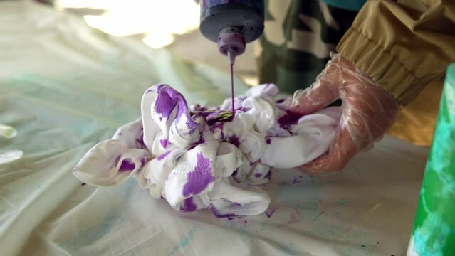 Painting of a white Tshirt with the help of purple paint. Staining Tshirts with your own hands Tie Dye. Video close -up of a person s hands.