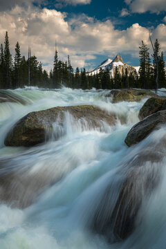 High in the Yosemite back country, the Tuolumne River rages down rocky rapids in spring with Cathedral Peak in the distance. California, USA.
