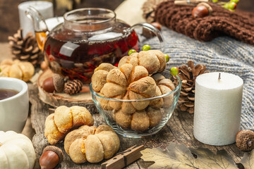 Autumn tea concept. Cookies with pumpkin puree, black tea in a glass teapot, fall decor