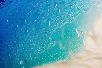 Drops of water and snow-white beach sand on blue glass. Abstract summer background