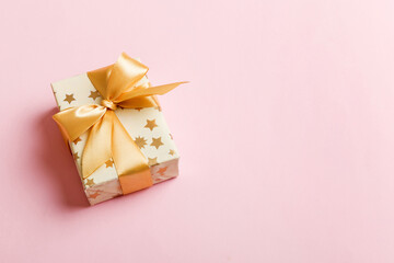 wrapped Christmas or other holiday handmade present in white paper with gold ribbon on colored background. Present box, decoration of gift on colored table, top view with copy space