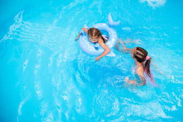 Two sister girls of 11-13 and 6 years old swim in a pool with blue water and have a fan. The older...