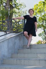 Middle-aged woman stands on the stairs in the park in summer