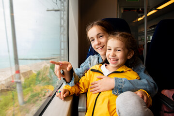 Two sister girls look out the window of a train at the sea.The girls are talking and having fun. Journey. Reflection. Vacation. Summer. Family vacation.