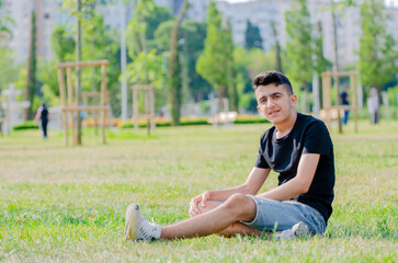 Fototapeta premium Handsome young boy in black shirt. Happy young male smiling on the grass in the park.