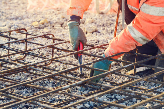 Builder's hands fixing steel reinforcement bars at construction site. Steel fixer assembling reinforcement cage. Selective focus