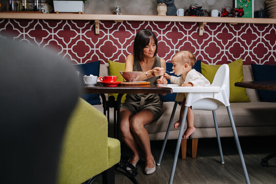 Low angle long shot image of a mother feeding her baby with a spoon in a cafe