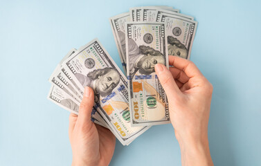 Female hands counting 100 dollar bills isolated on a blue background.